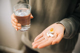 a woman holding supplements in one hand and a glass of water in the other hand