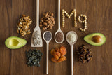 Magnesium-rich foods on a wood surface, including avocado, dried fruits, nuts, and seeds