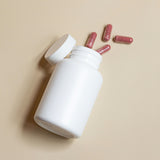 supplement capsules coming out of a white bottle on beige background