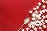 sugar cubes and sugar on a spoon on a red background