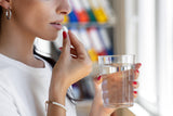 woman with a glass of water about to take a vitamin