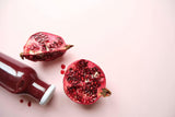 half a pomegranate, a quarter of a pomegranate, and bottle pomegranate juice on a very light red background