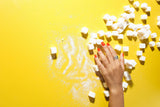 sugar cubes on a bright yellow background with a woman's hand over some of the cubes