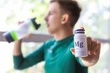 man drinking water from a bottle and holding a magnesium pill bottle