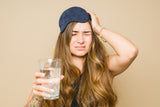 woman with a sleep mask has a headache and is holding a glass of water