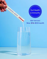 Hand pouring a supplement stick pack labeled 'Modern Dose Biotic Blend' into a glass of water with a blue background and 'Gut Health & Immunity' text.
