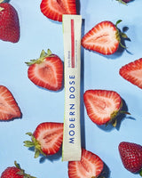 Modern Dose Biotic Blend supplement stick pack surrounded by sliced strawberries on a blue background - www.moderndose.com