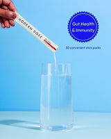 Hand pouring a supplement stick pack labeled 'Modern Dose Biotic Blend' into a glass of water with a blue background and 'Gut Health & Immunity' text.