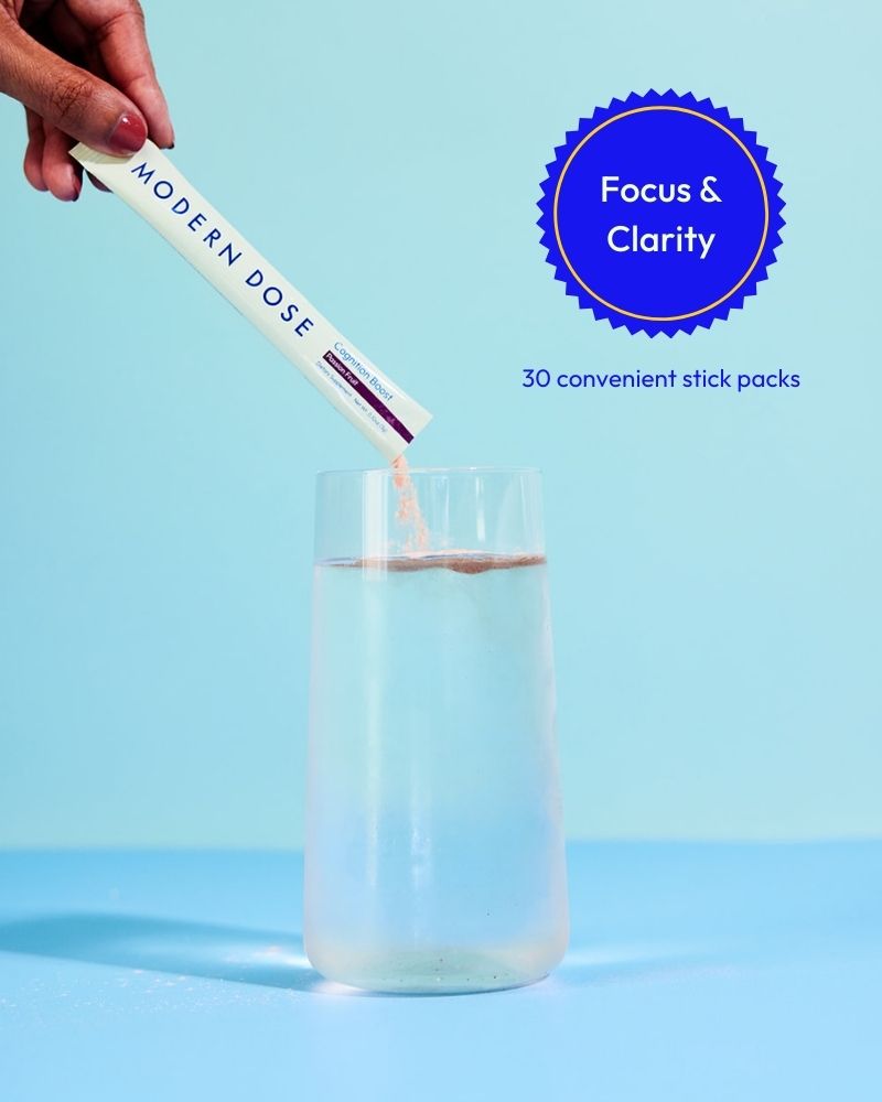 Modern Dose Cognition Boost supplement stick pack being added to a glass of water with a blue background and text about focus & clarity