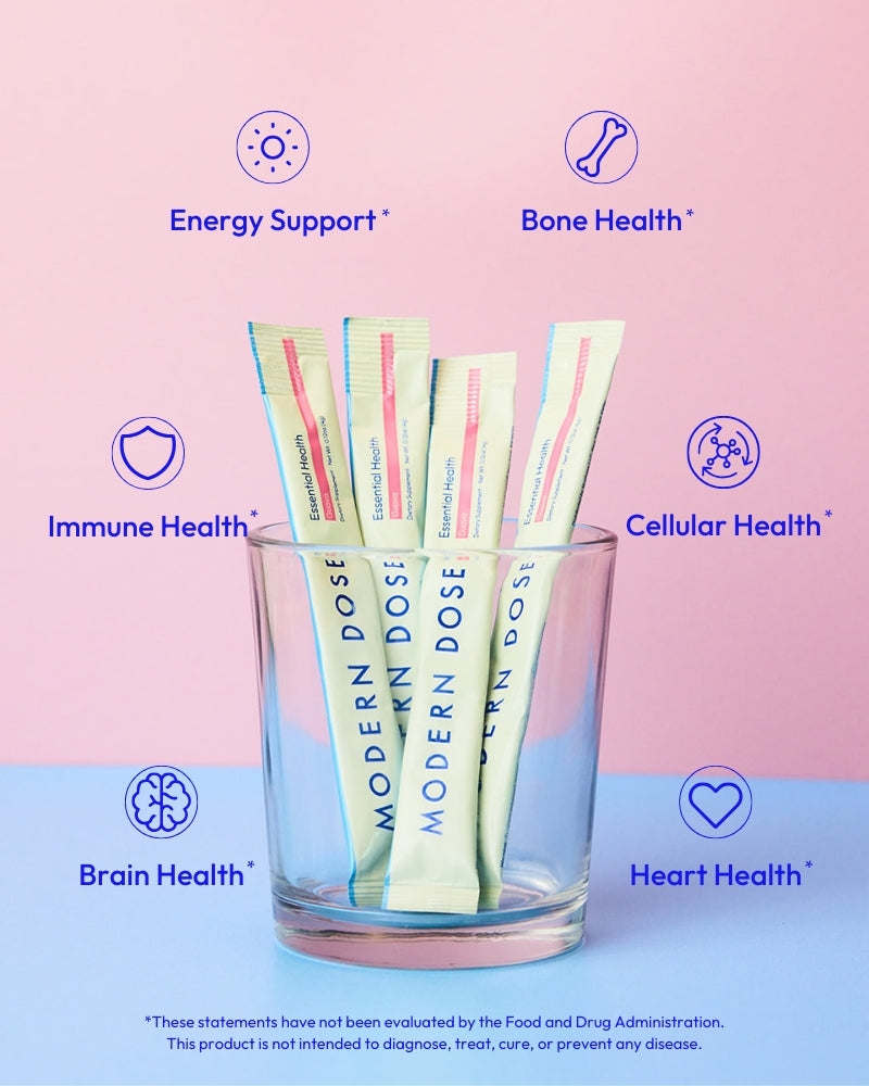 Glass with Modern Dose Essential Health supplement packets labeled for health benefits on a pink and blue gradient background