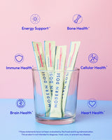 Glass with Modern Dose Essential Health supplement packets labeled for health benefits on a pink and blue gradient background