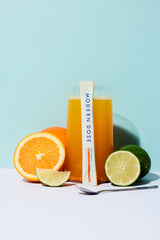 Citrus Joint Support drink with Modern Dose stick pack leaning against it, surrounded by limes and oranges on a blue background - www.moderndose.com