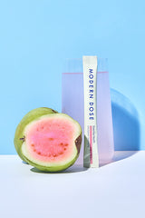 Modern Dose Essential Health drink with stick pack leaning against the glass and next to a guava on a light blue background - www.moderndose.com