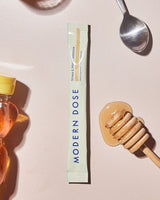 Modern Dose supplement stick pack with honey and a spoon on a light background