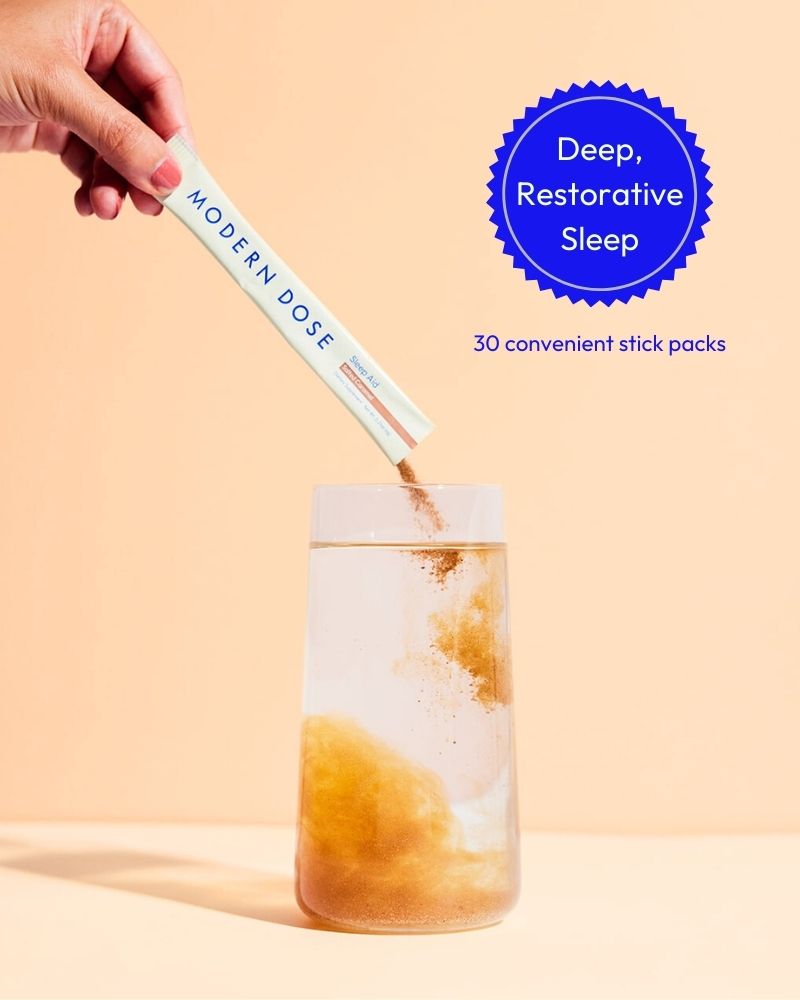 Hand holding a stick pack labeled 'Modern Dose' and pouring it into a glass of water with a 'Deep Restorative Sleep' label on the background.