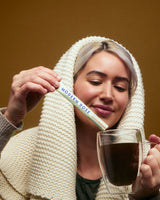 Woman holding a glass of Modern Dose Sleep Aid supplement and a 'Modern Dose' supplement stick pack against a brown background - www.moderndose.com