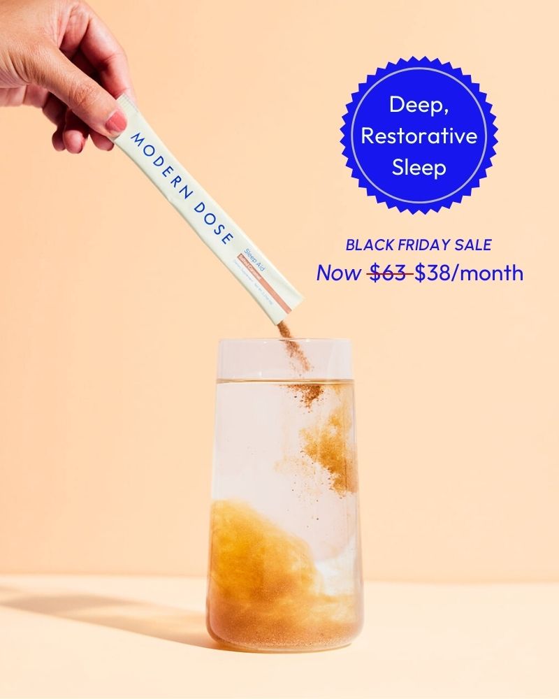 Hand holding a stick pack labeled 'Modern Dose' and pouring it into a glass of water with a 'Deep Restorative Sleep' label on the background. Black Friday Promotion